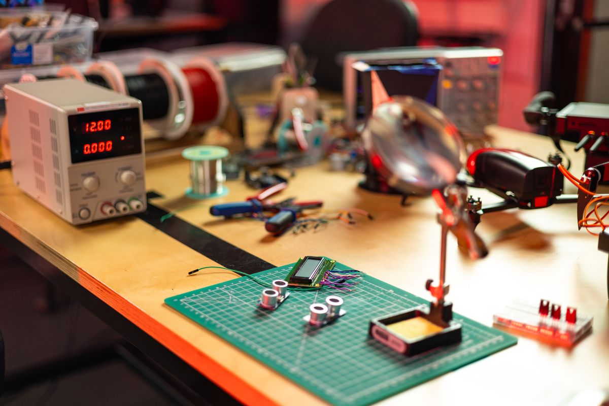 A workbench with a bench power supply, spools of wire, small sensor boards laid out on a cutting mat, and an oscilloscope behind them