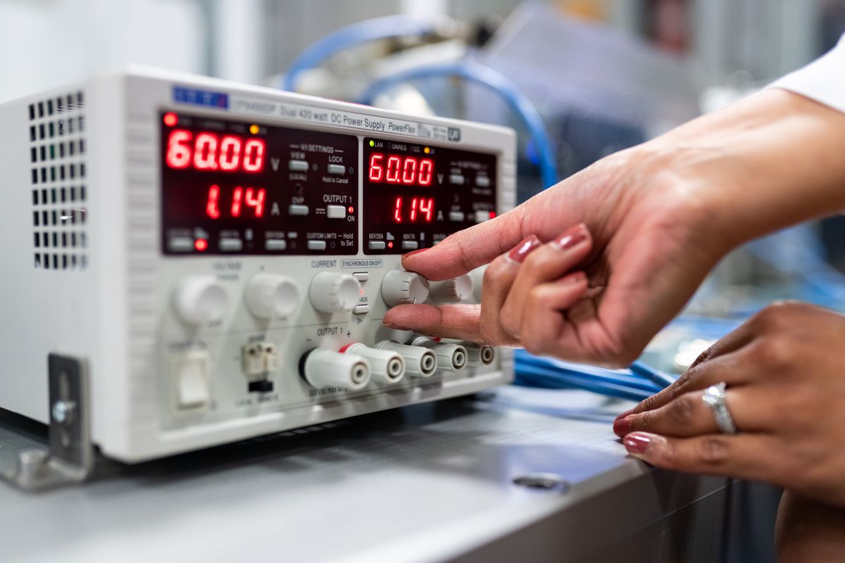 A bench power supply showing a voltage and a current reading while a hand adjusts the current control
